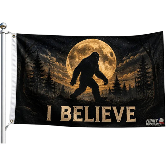 A novelty flag featuring a silhouette of Bigfoot walking in a forest under a large full moon, with the text 'I BELIEVE' at the bottom. The flag is shown hanging from a white flagpole against a plain white background.